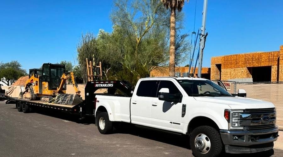 NexGen Auto Transport providing reliable equipment delivery service with a covered trailer unloading machinery at a commercial site.