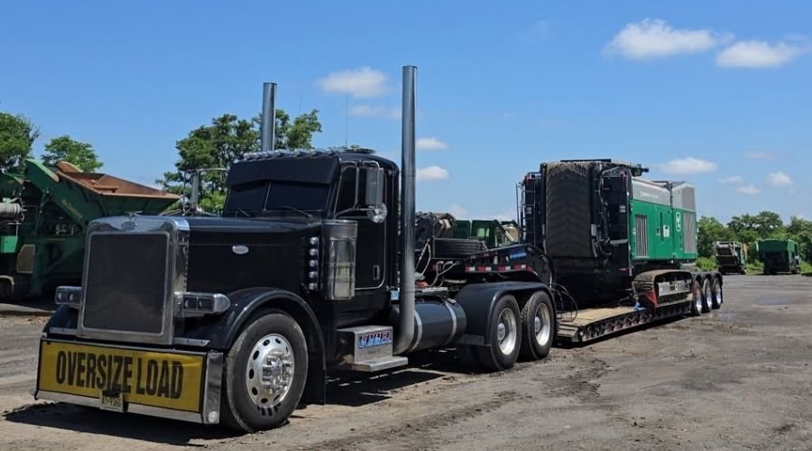 NexGen Auto Transport managing heavy machine transport with a lowboy trailer hauling oversized industrial equipment through a logistics route.